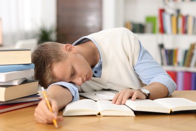 Photo of Preparing for exam. Tired student sleeping among books at table indoors