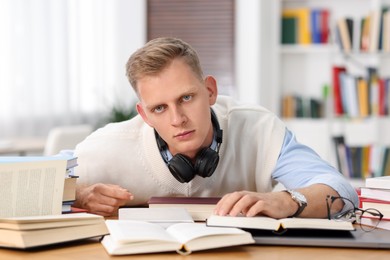 Photo of Preparing for exam. Tired student with books at table indoors