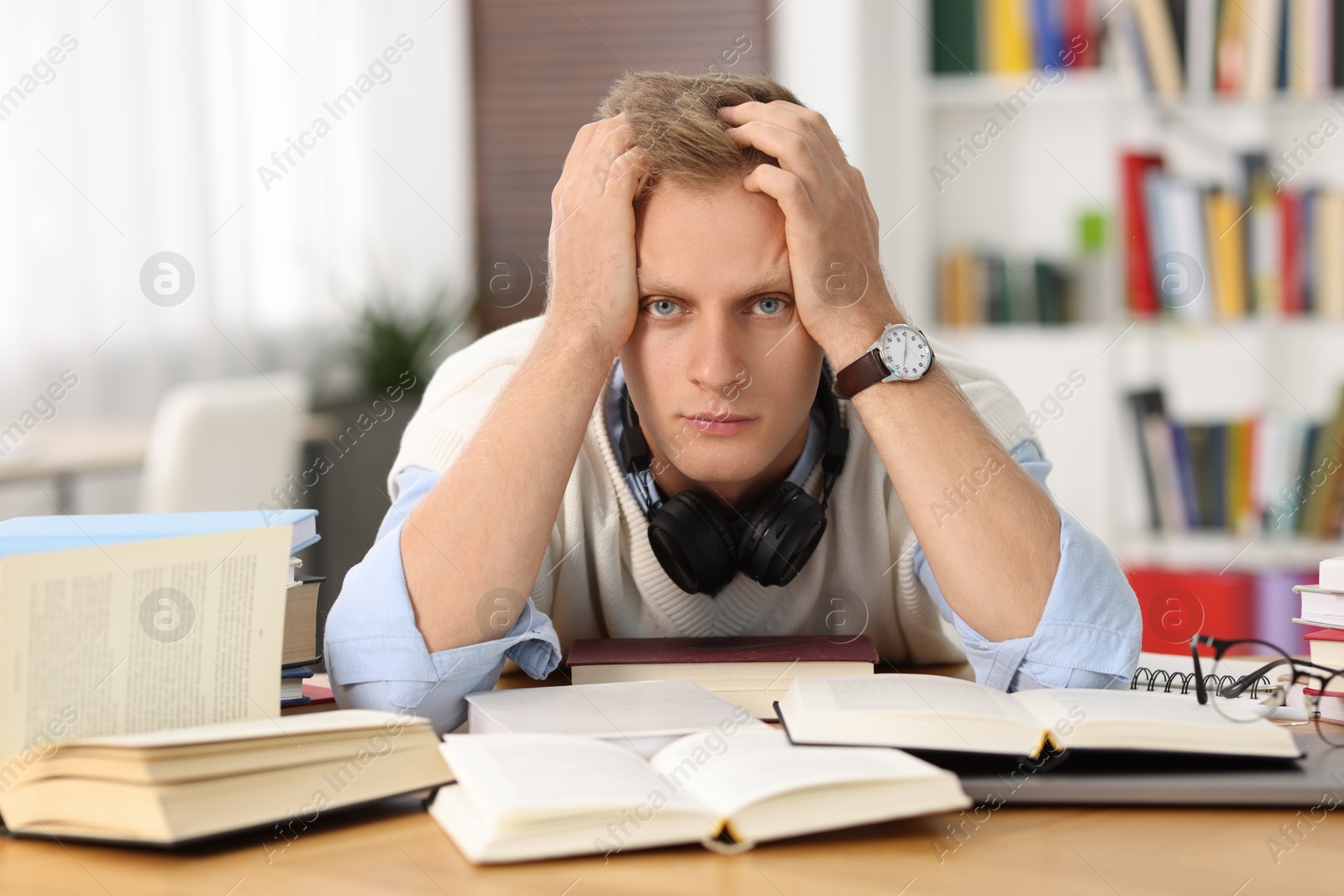 Photo of Preparing for exam. Tired student with books at table indoors