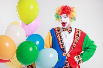 Photo of Emotional clown with colorful balloons on light background