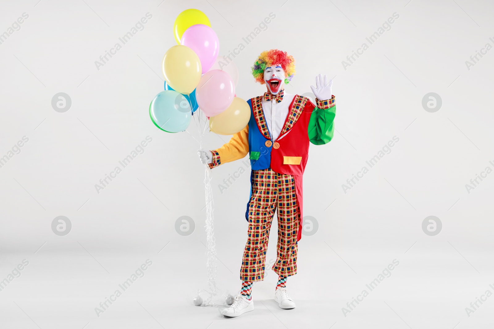 Photo of Happy clown with colorful balloons waving on light background