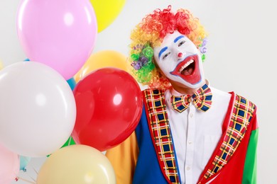 Photo of Happy clown with colorful balloons on light background