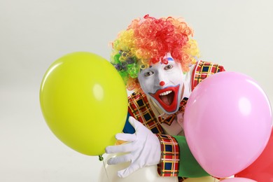 Photo of Emotional clown with colorful balloons on light background