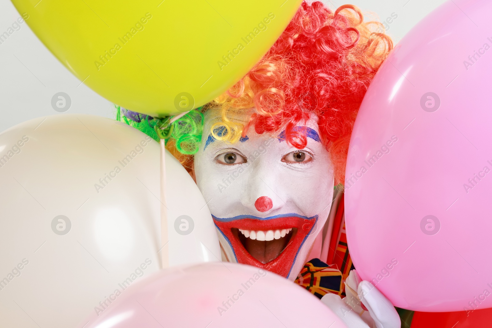 Photo of Happy clown with colorful balloons on light background