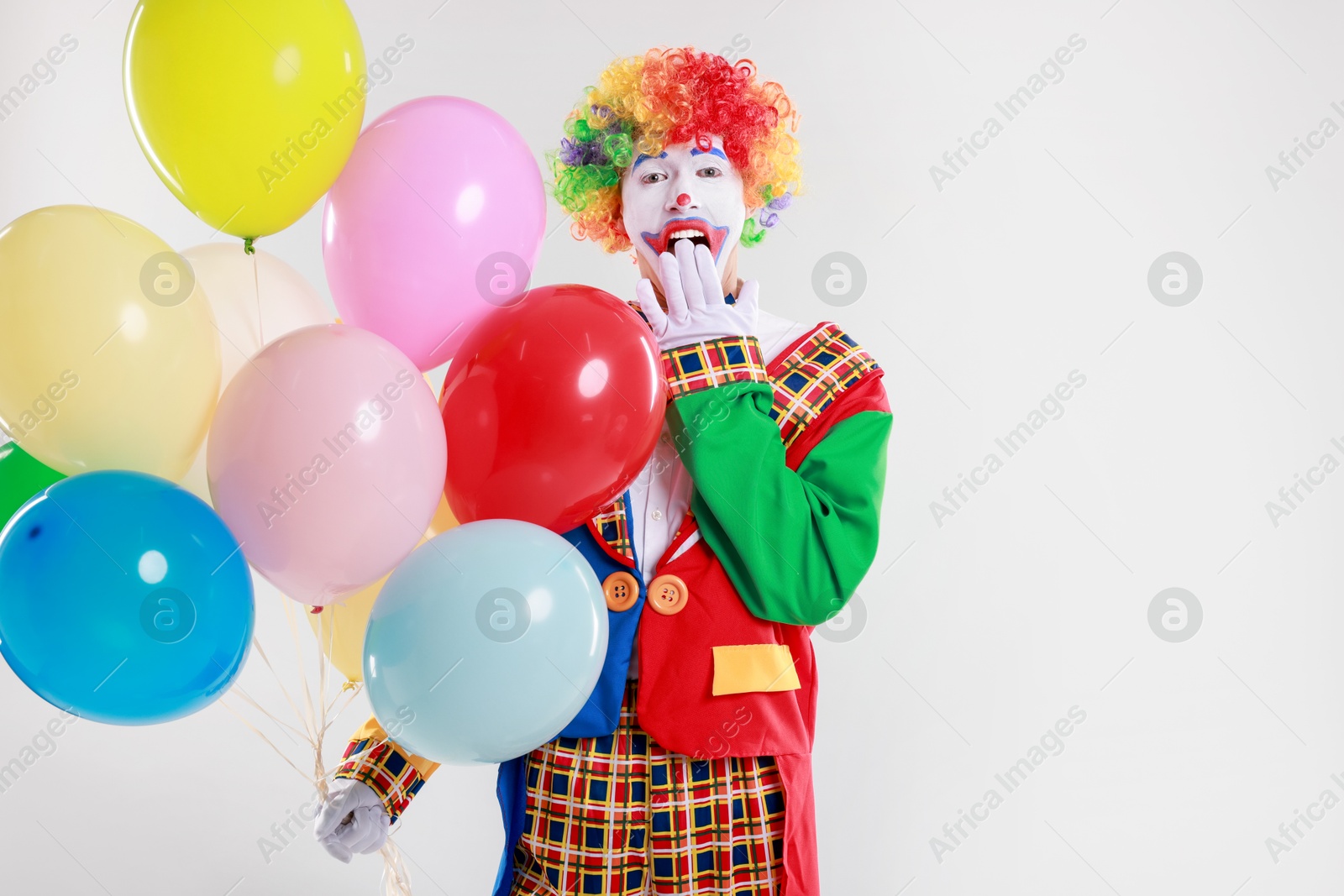 Photo of Emotional clown with colorful balloons on light background, space for text