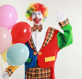 Happy clown with colorful balloons on light background