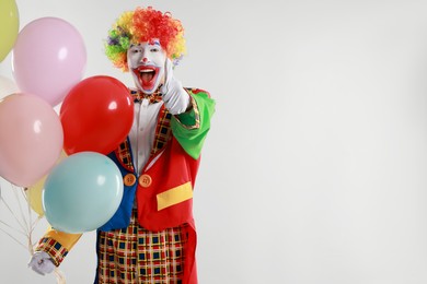 Photo of Happy clown with colorful balloons showing thumbs up on light background, space for text