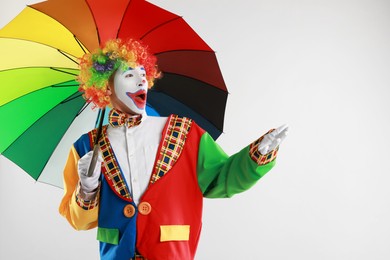 Emotional clown with colorful umbrella on light background, space for text