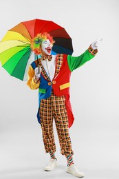 Photo of Happy clown with colorful umbrella on light background