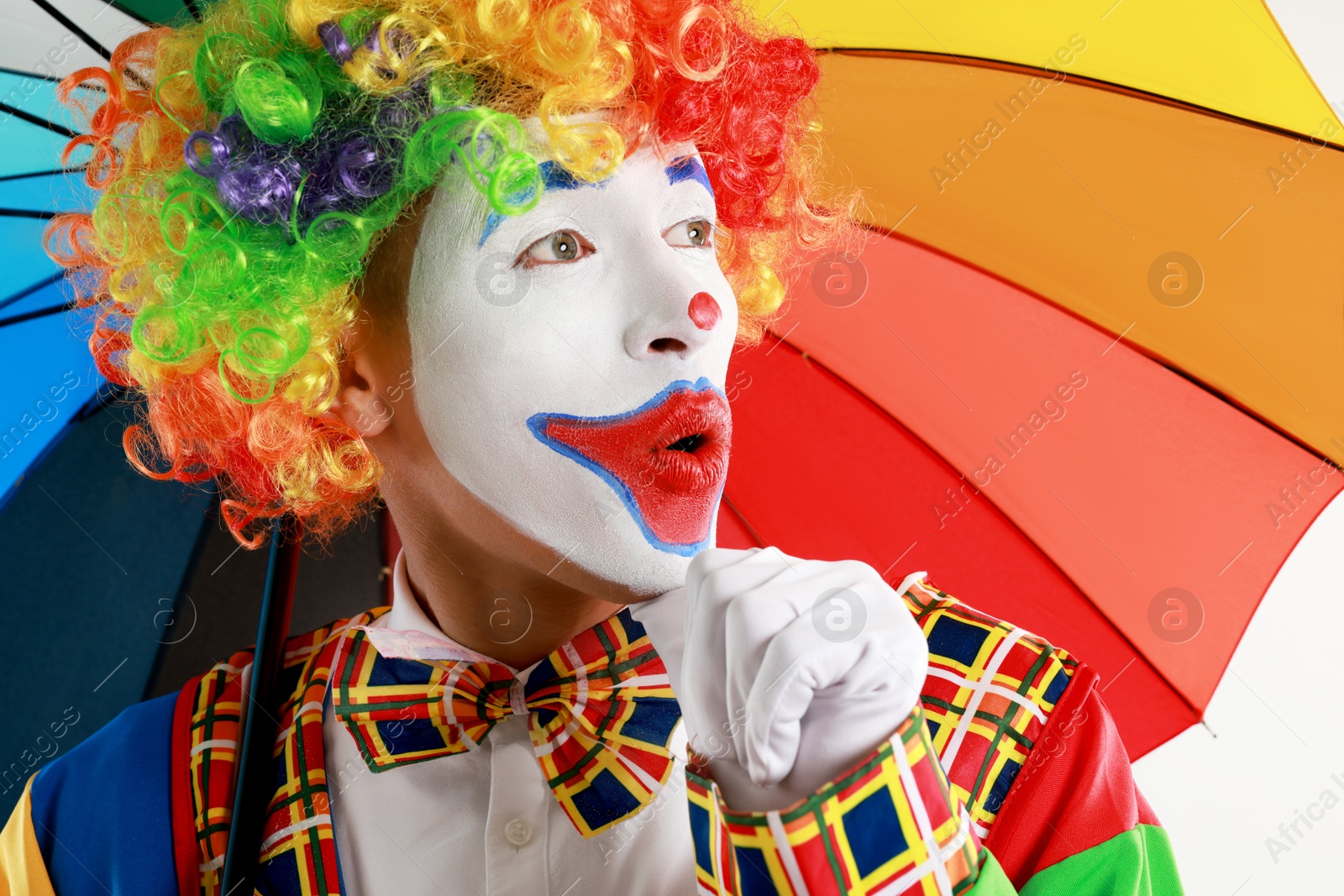 Photo of Emotional clown with colorful umbrella on light background