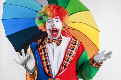 Emotional clown with colorful umbrella on light background