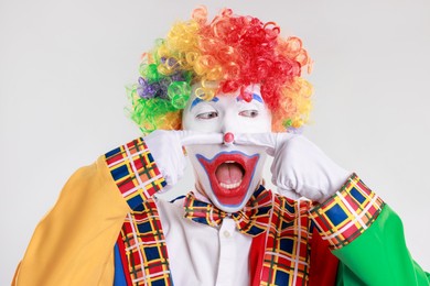 Photo of Emotional clown touching his nose on light background