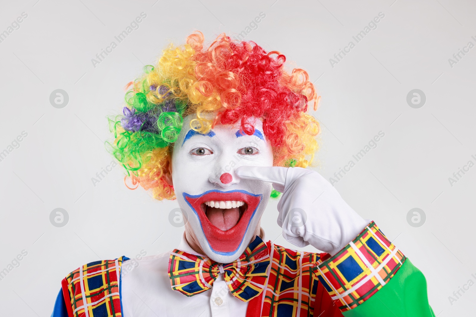 Photo of Emotional clown touching his nose on light background