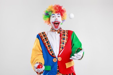 Photo of Funny clown juggling balls on light background