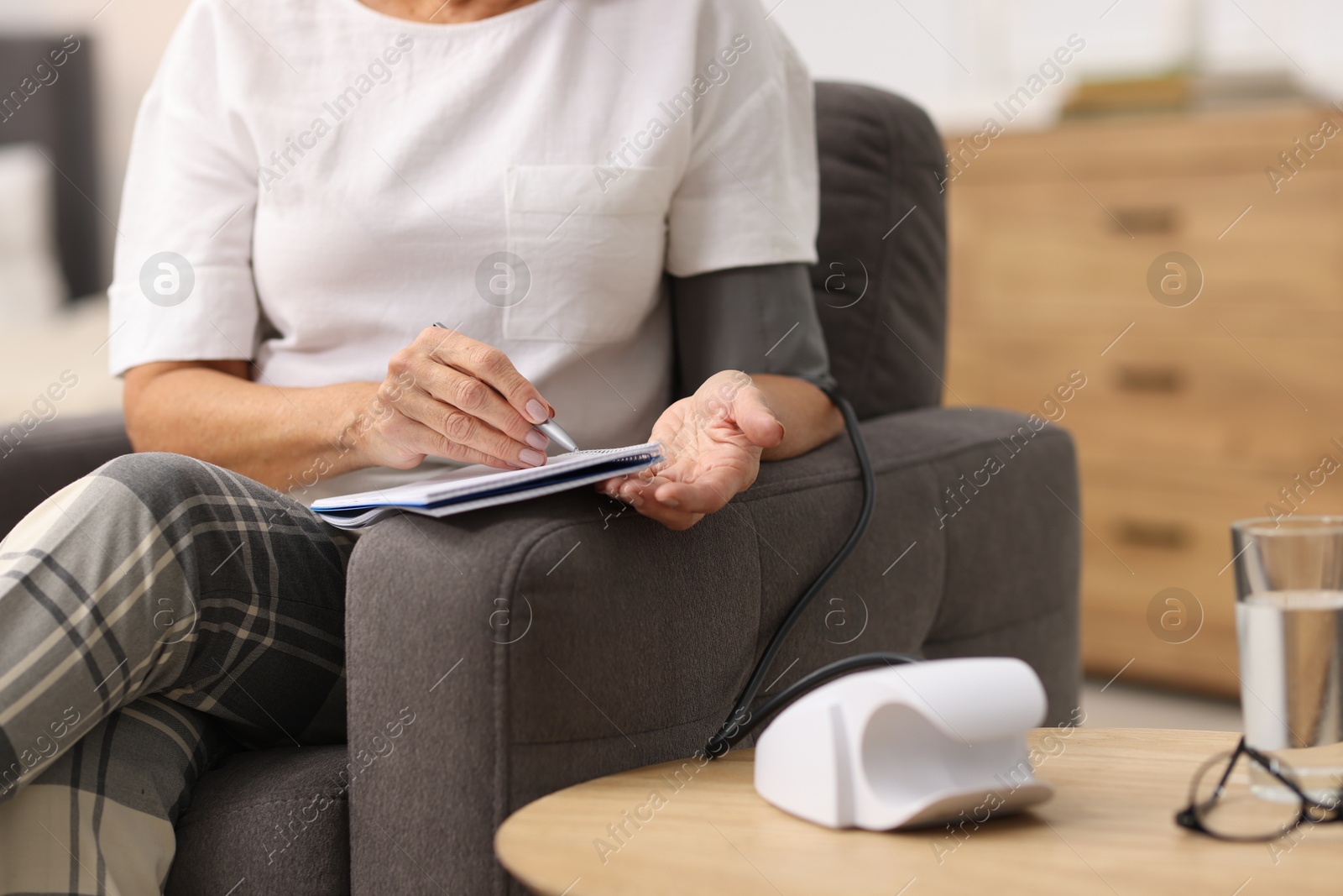 Photo of Senior woman writing results of blood pressure measurement at home, closeup