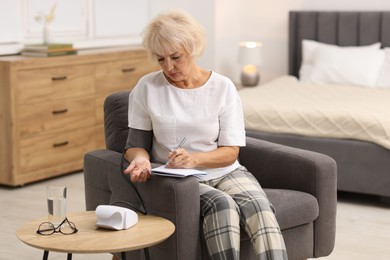 Photo of Senior woman writing results of blood pressure measurement at home