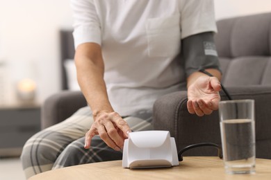 Photo of Senior woman measuring blood pressure in armchair at home, closeup