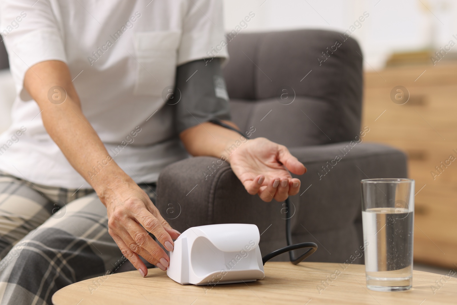 Photo of Senior woman measuring blood pressure in armchair at home, closeup