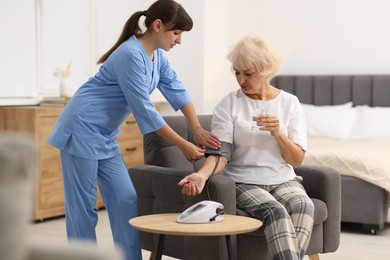 Photo of Nurse measuring senior woman's blood pressure at home