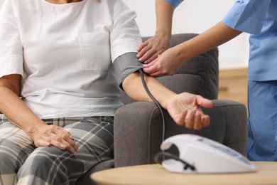 Photo of Nurse measuring senior woman's blood pressure at home, closeup