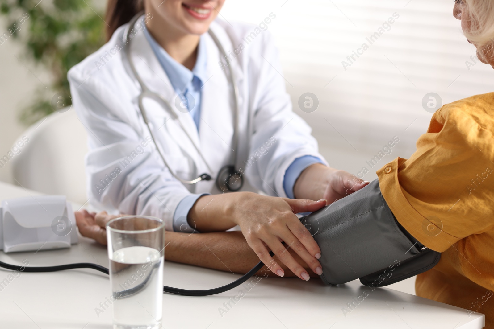 Photo of Doctor measuring senior woman's blood pressure during appointment in hospital, closeup