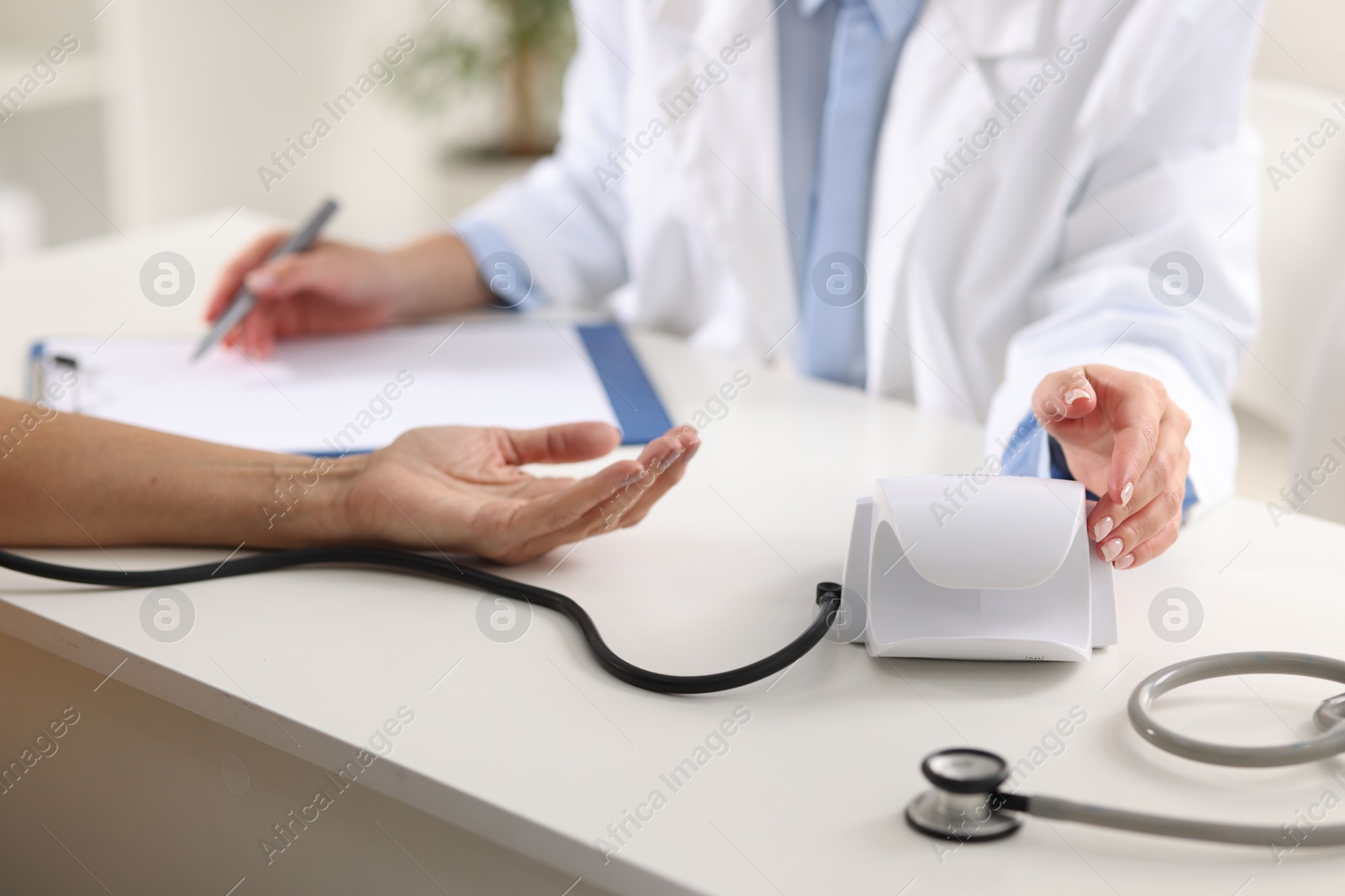 Photo of Doctor measuring senior woman's blood pressure and writing results in hospital, closeup