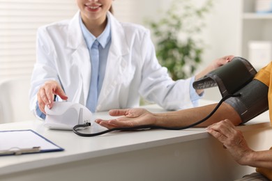 Doctor measuring senior woman's blood pressure during appointment in hospital, closeup