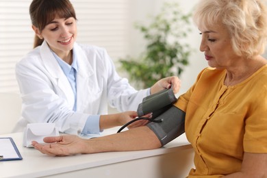 Photo of Doctor measuring senior woman's blood pressure during appointment in hospital