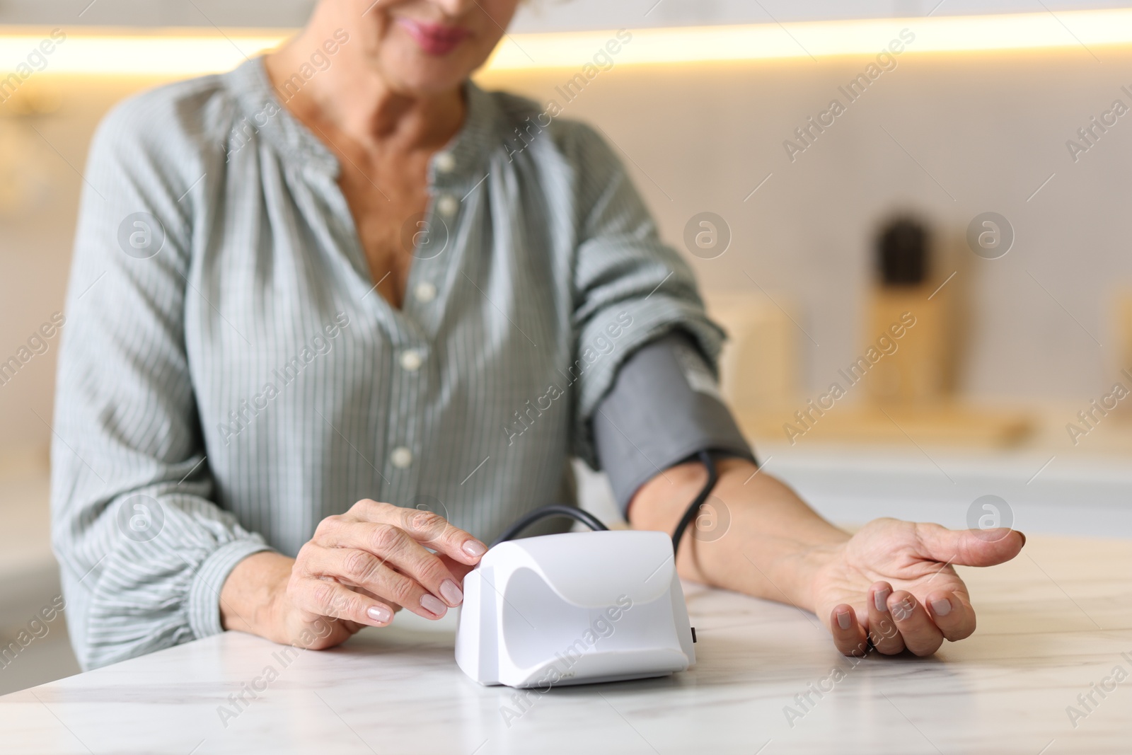 Photo of Senior woman measuring blood pressure at table in kitchen, closeup