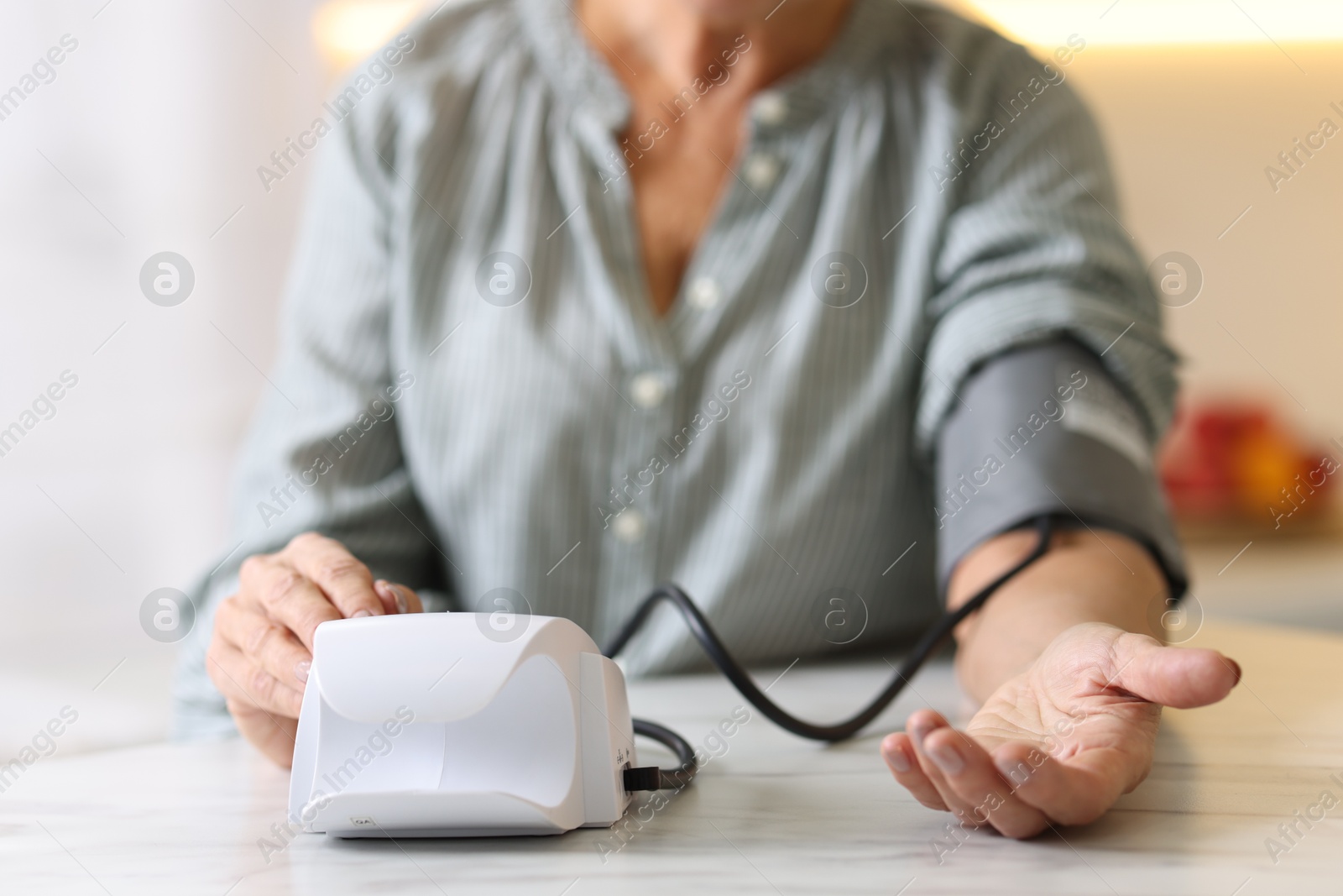 Photo of Senior woman measuring blood pressure at table in kitchen, closeup