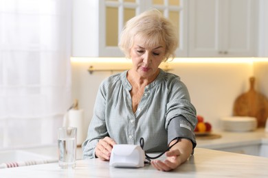 Photo of Senior woman measuring blood pressure at table in kitchen