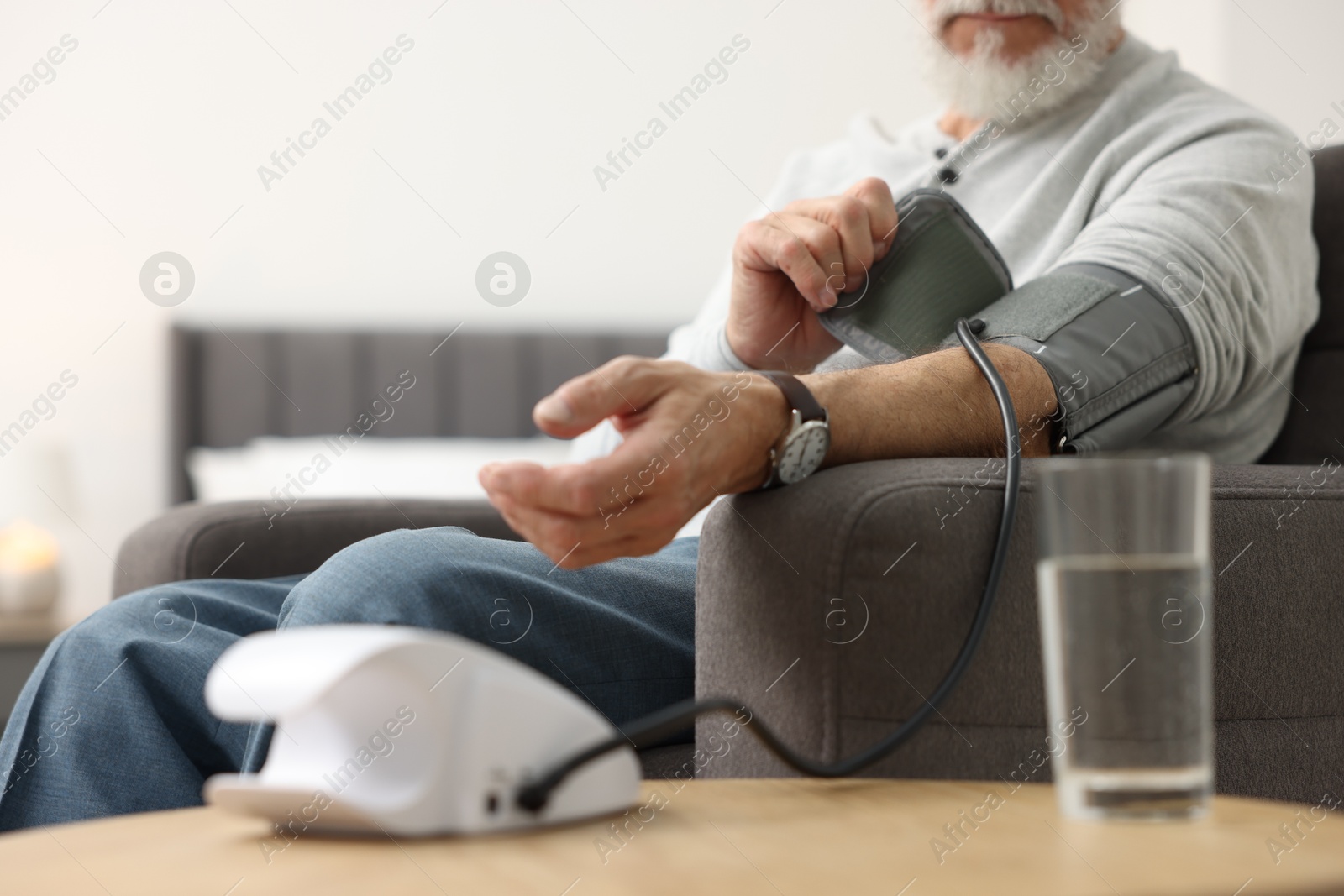 Photo of Senior man measuring blood pressure in armchair at home, closeup