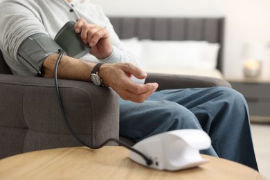 Photo of Senior man measuring blood pressure in armchair at home, closeup