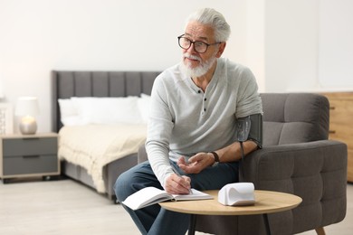 Photo of Senior man writing results of blood pressure measurement at home