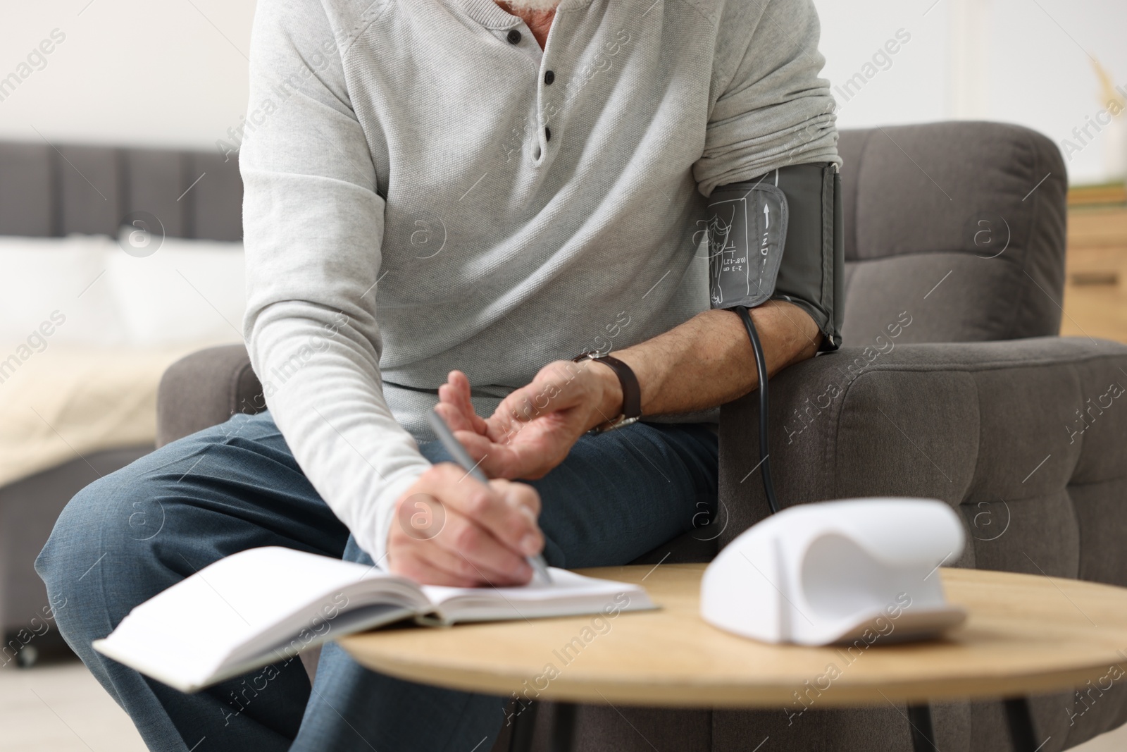 Photo of Senior man writing results of blood pressure measurement at home, closeup