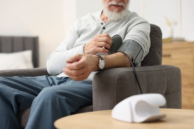 Photo of Senior man measuring blood pressure in armchair at home, closeup