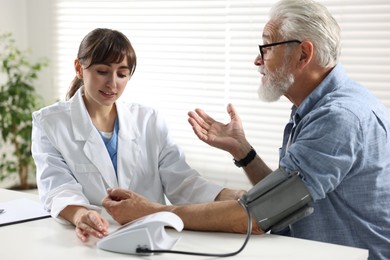 Photo of Doctor measuring senior man's blood pressure during appointment in hospital