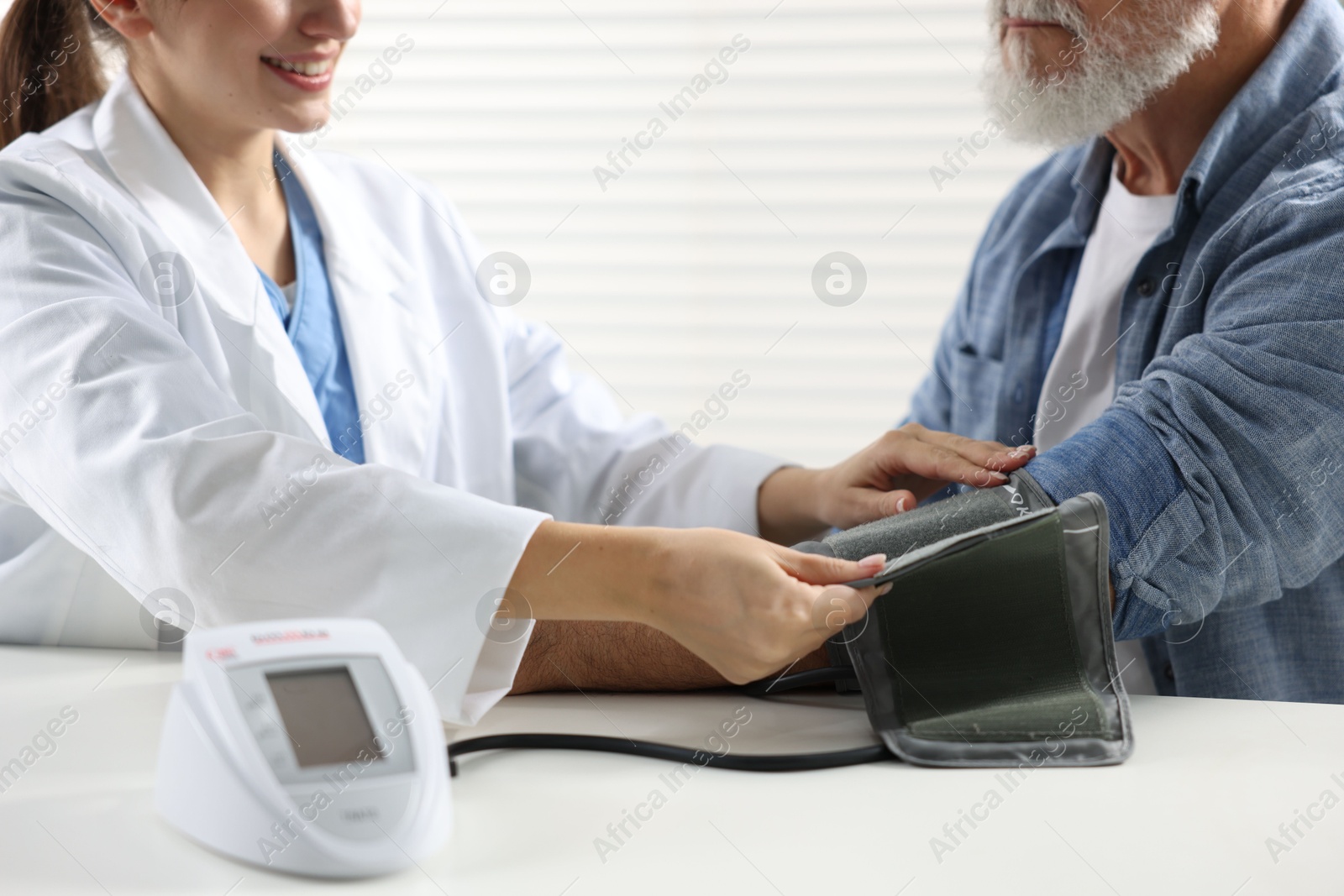 Photo of Doctor measuring senior man's blood pressure during appointment in hospital, closeup