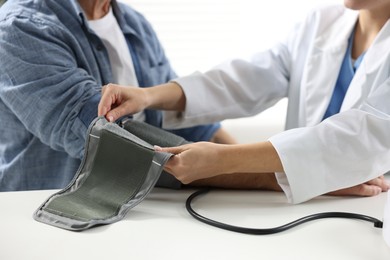 Photo of Doctor measuring senior man's blood pressure during appointment in hospital, closeup