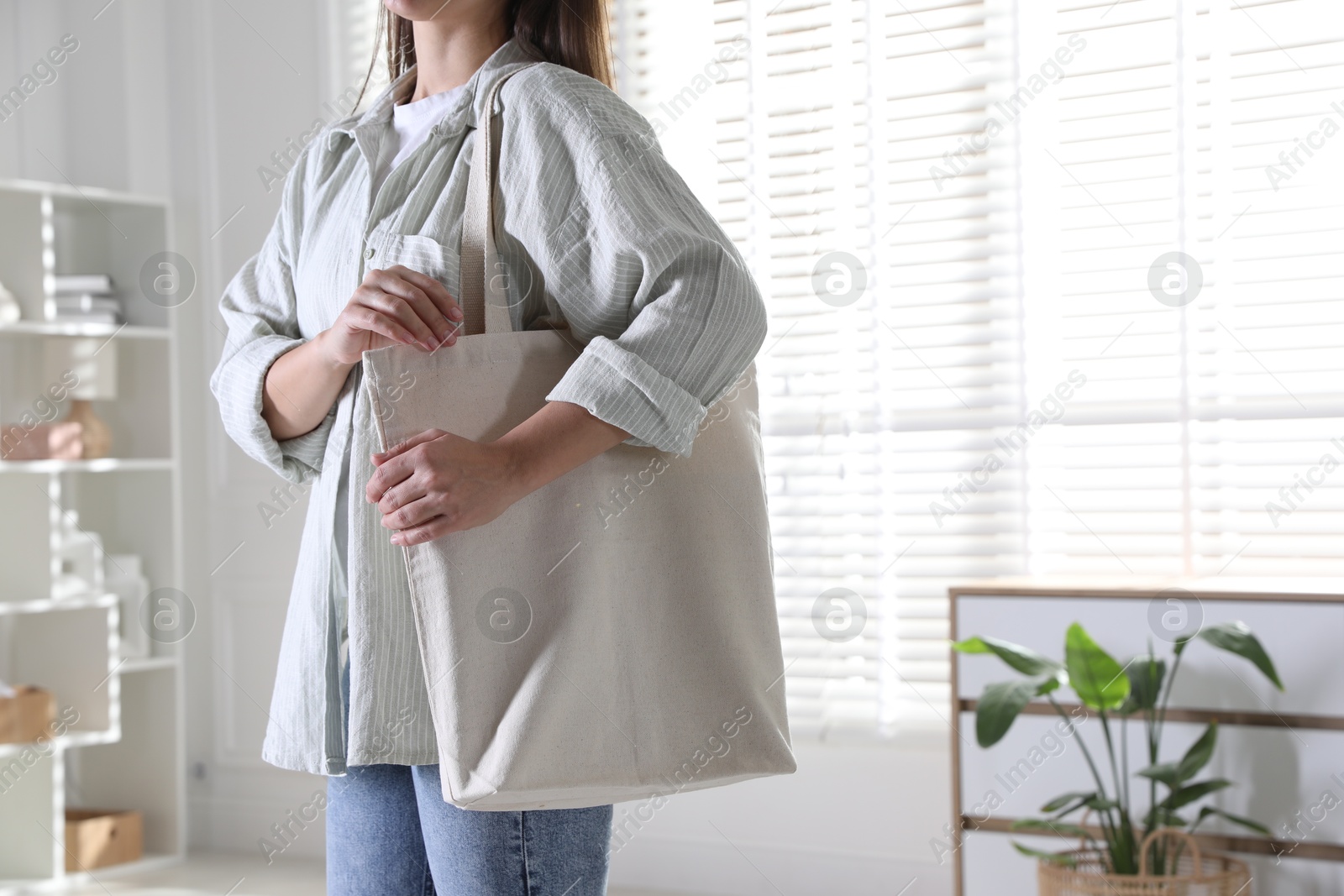 Photo of Woman with blank shopper bag indoors, closeup. Mockup for design