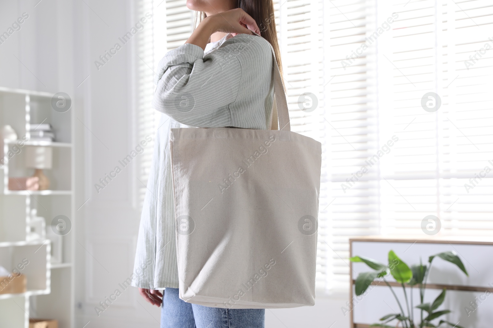 Photo of Woman with blank shopper bag indoors, closeup. Mockup for design