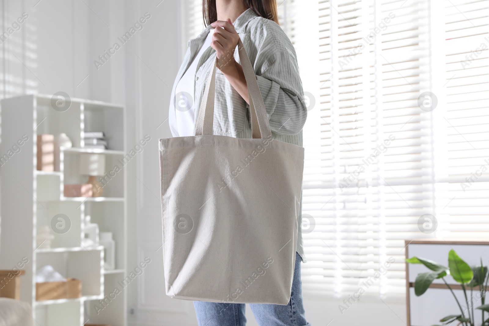 Photo of Woman with blank shopper bag indoors, closeup. Mockup for design