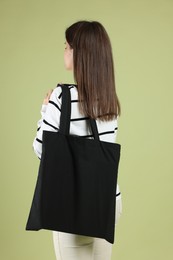 Photo of Woman with blank black shopper bag on color background, back view. Mockup for design