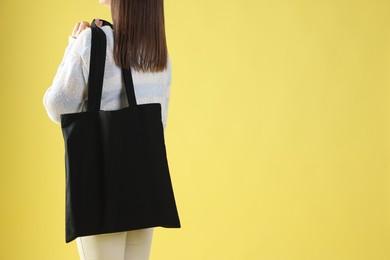 Photo of Woman with blank black shopper bag on yellow background, back view. Mockup for design