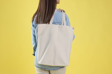 Photo of Woman with blank shopper bag on yellow background, back view. Mockup for design