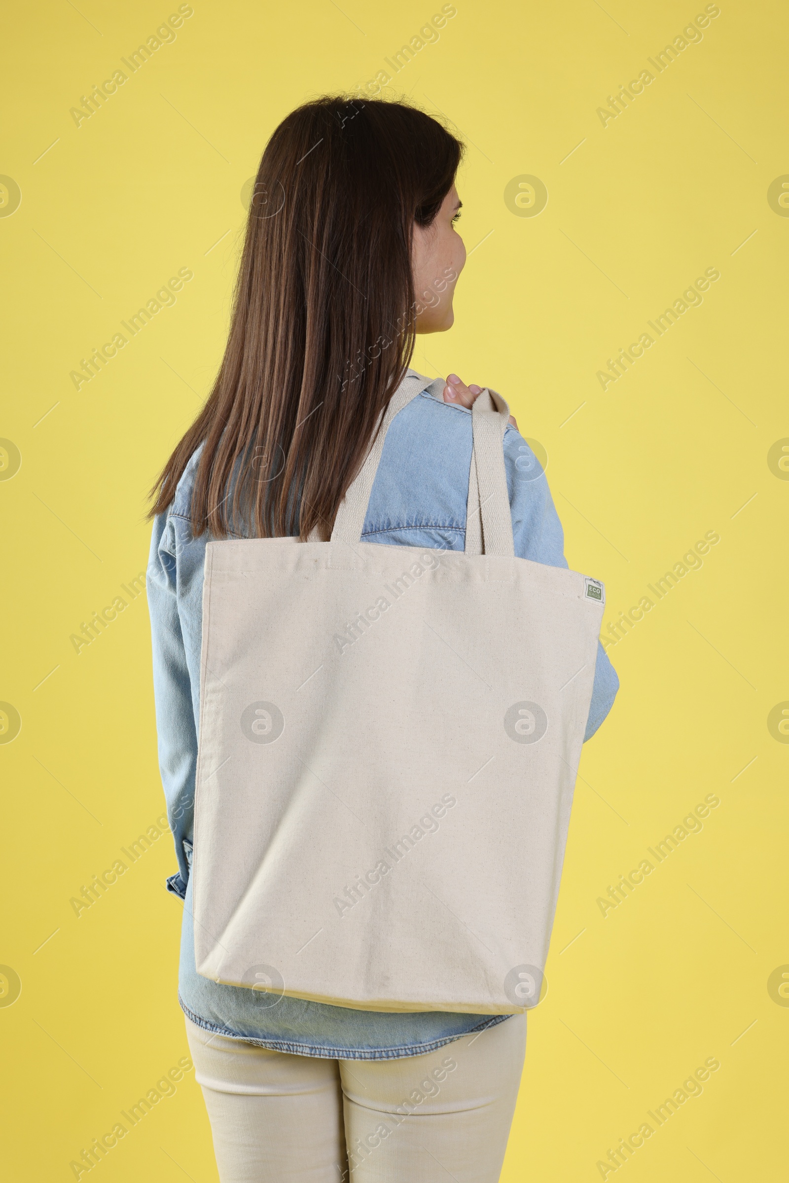 Photo of Woman with blank shopper bag on yellow background, back view. Mockup for design