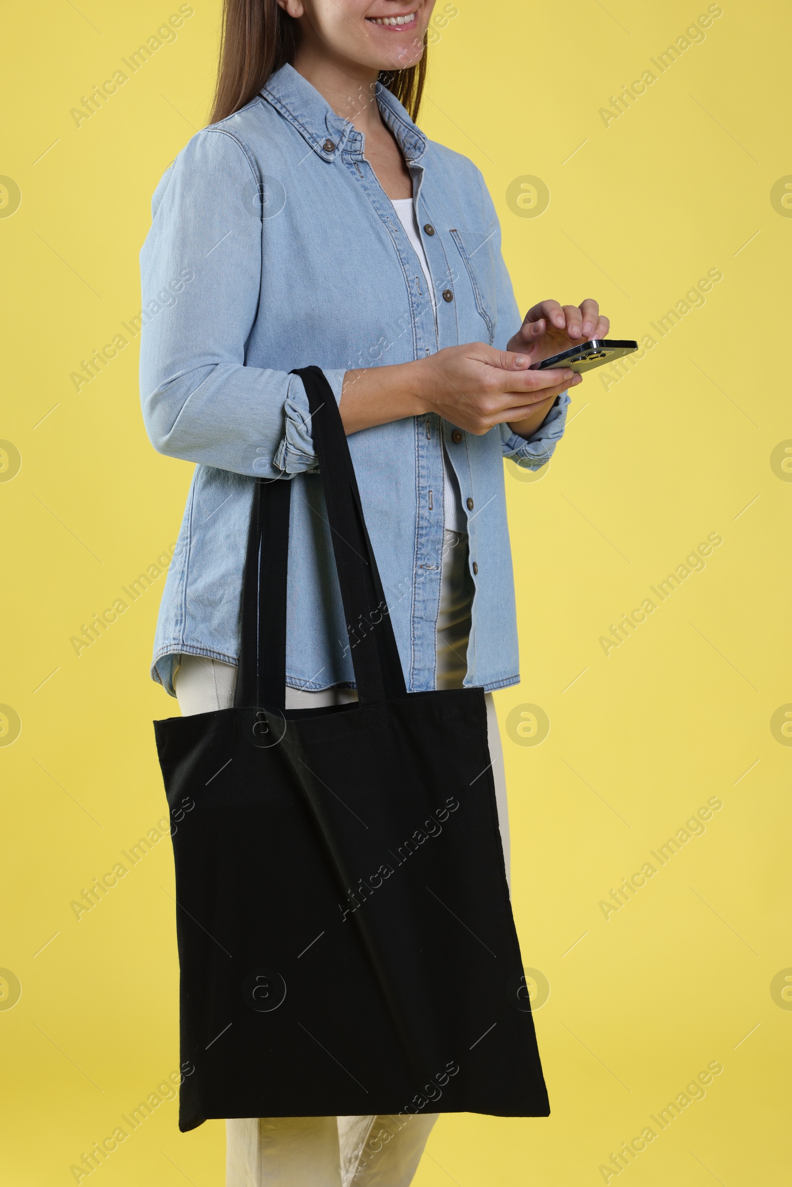 Photo of Woman with blank black shopper bag on yellow background, closeup. Mockup for design