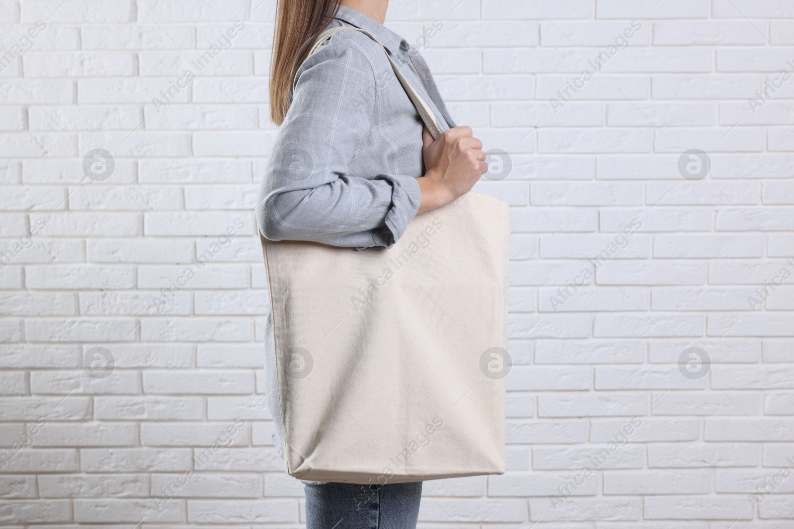 Photo of Woman with blank shopper bag near white brick wall, closeup. Mockup for design