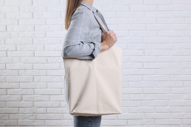 Photo of Woman with blank shopper bag near white brick wall, closeup. Mockup for design