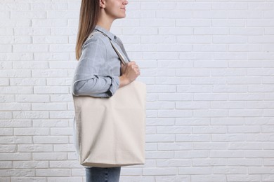 Photo of Woman with blank shopper bag near white brick wall, closeup. Mockup for design